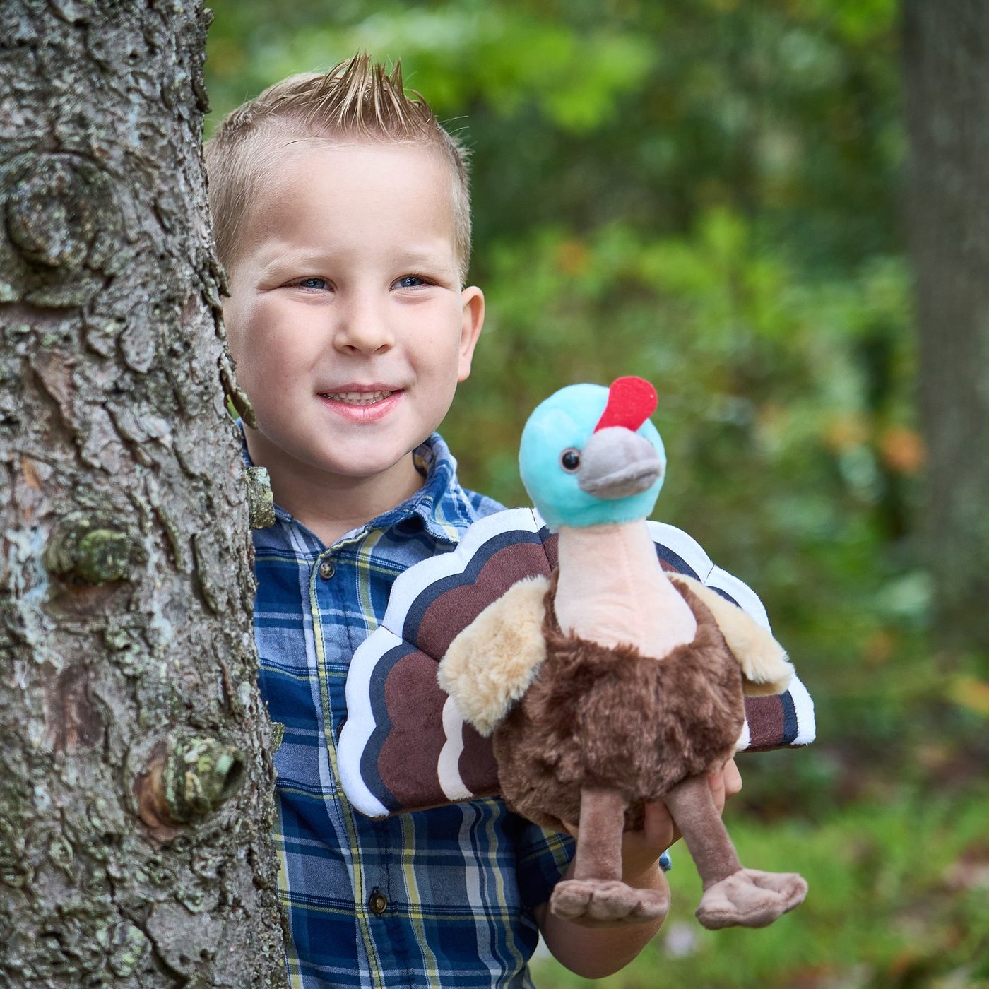 A boy by a tree holding a brightly coloured bird plush toy