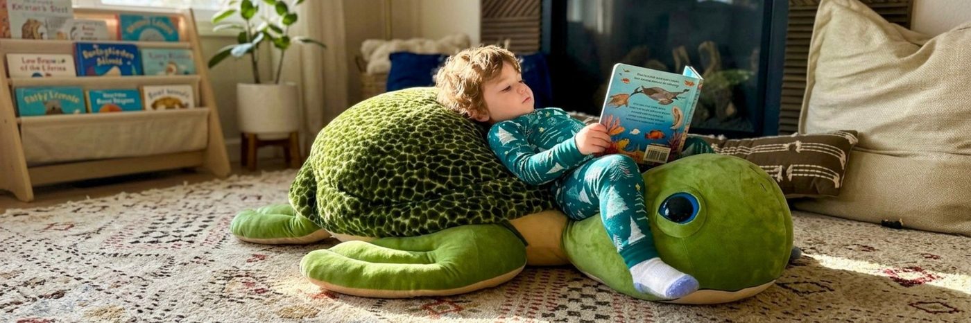 A child clambering over a green sea turtle jumbo plush toy