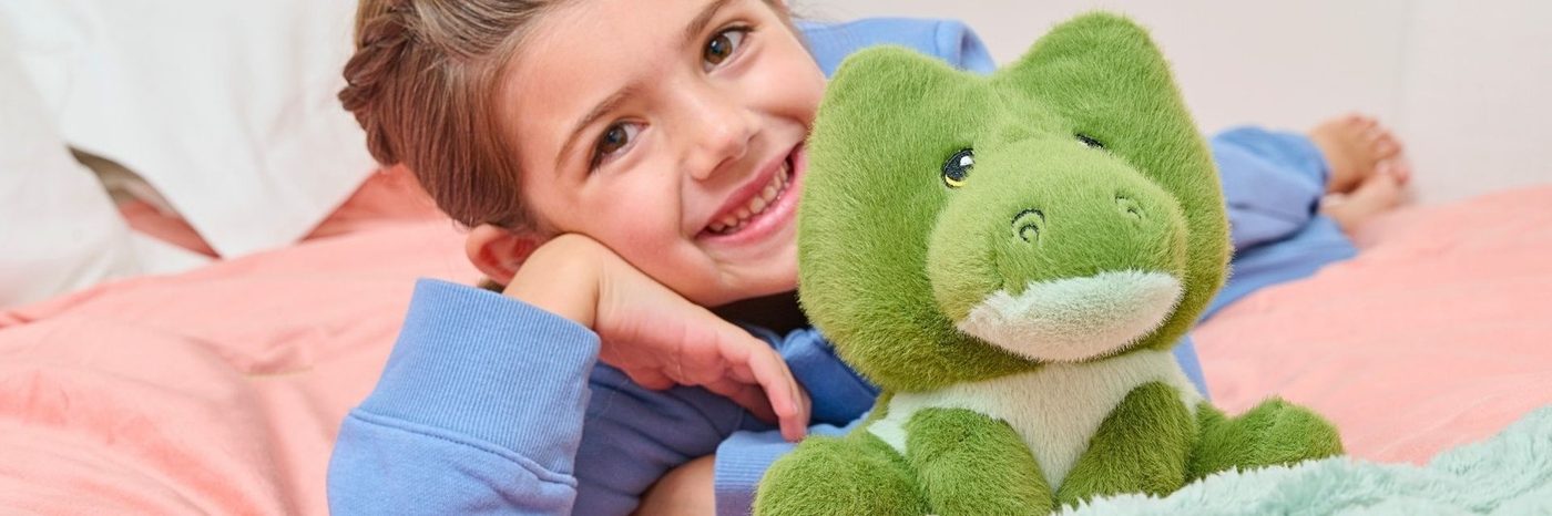 A child in bed holding a green frog plush toy