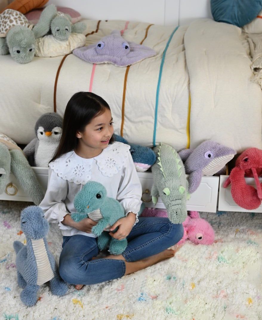 A girl sitting on a rug with a fan of pastel Zoologee plush toys