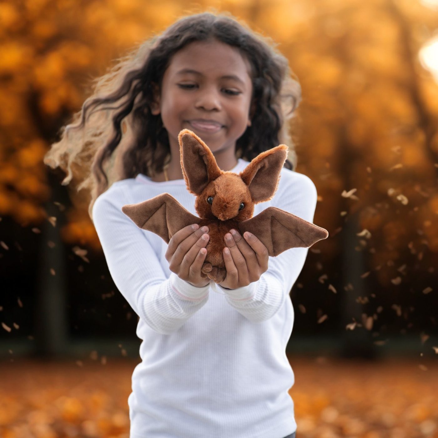 A girl throwing autumn leaves while holding a brown plush animal