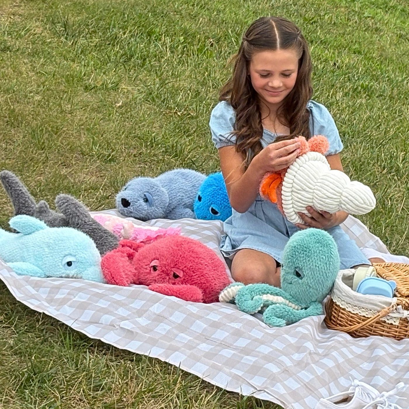 A girl kneeling on a picnic blanket covered with rounded Zoologee plush animals