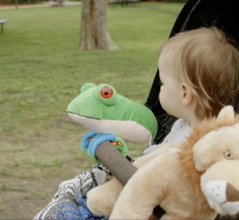 A toddler in a stroller holding a green frog plush toy