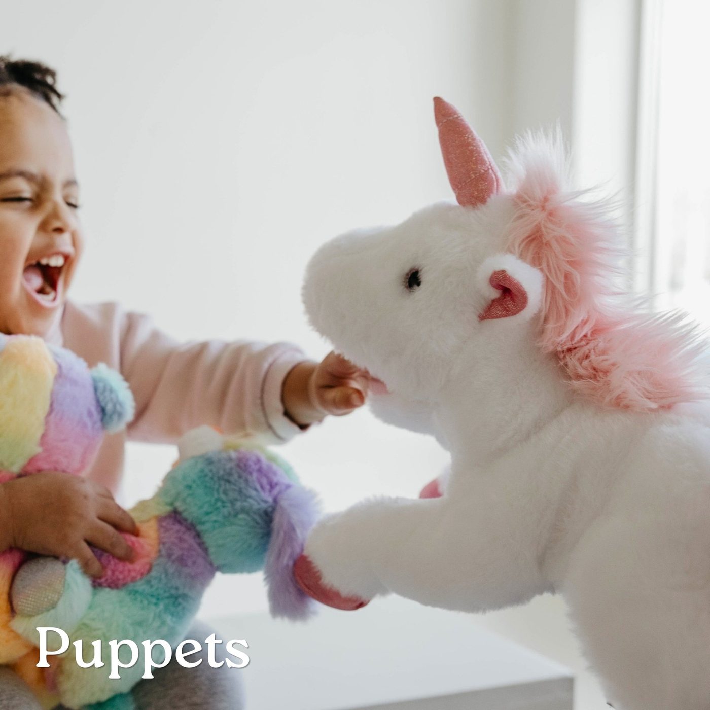 A laughing toddler reaching for a unicorn plush hand puppet